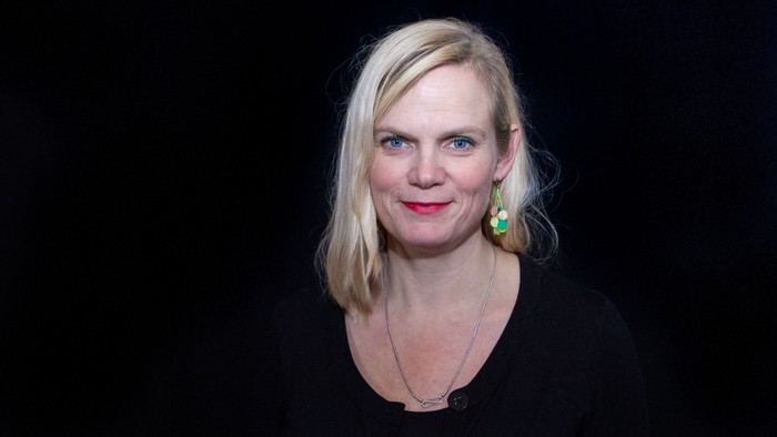 En kvinde med blondt hår, der bærer sorte og grønne øreringe.