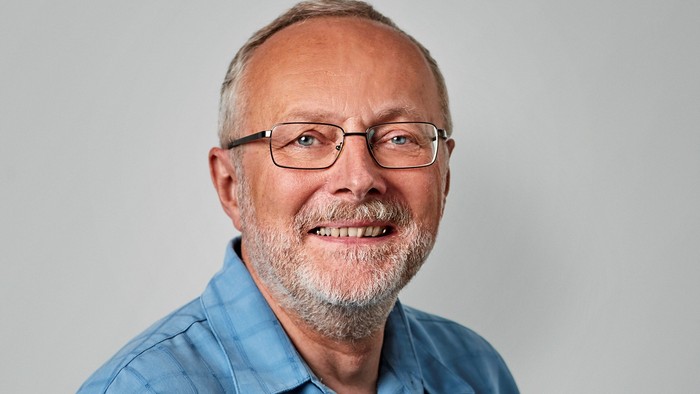 Mand i middelalderen med briller og skæg, iført en blå skjorte.