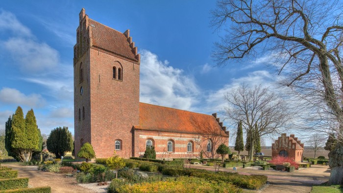 En rød murstenskirke med tårn og omgivelser