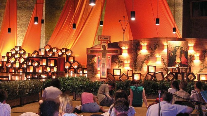 Open-Air-Kulturevent mit beleuchteter Bühne, traditionellen Darbietungen und sitzendem Publikum unter lebhaften roten Vorhängen.