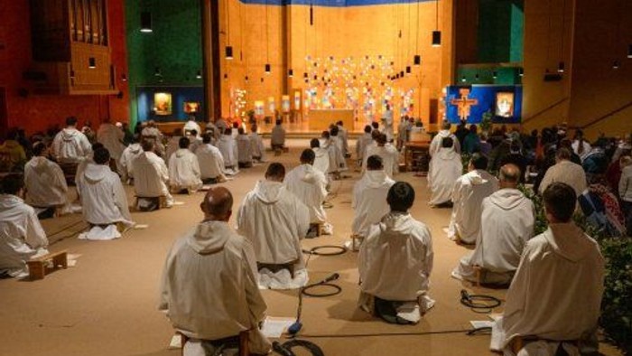 Eine Gruppe von Menschen in weißen Roben sitzt in einem Raum und meditiert.