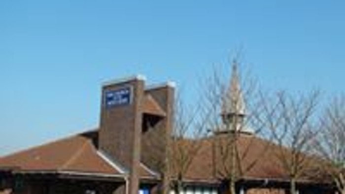 A large building with a sign on top, surrounded by trees and a parking lot.