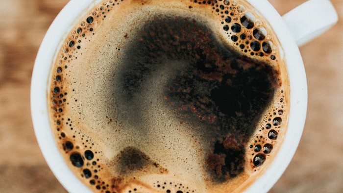 Et nærbillede af en latte art-kaffe med et hjerteformet skumdesign i en hvid kop på et træunderlag.