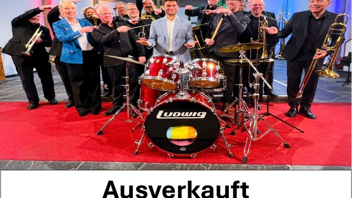 Eine ausverkaufte Band tritt auf der Bühne mit Blechblasinstrumenten und Schlagzeug auf und zeigt die Marke Ludwig auf den Trommeln.