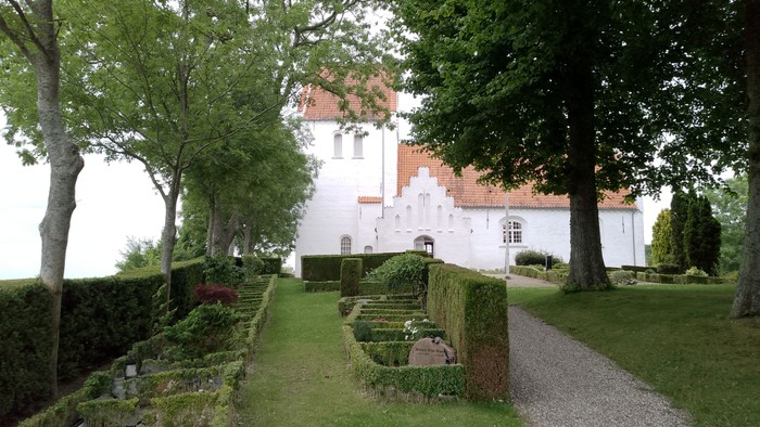 En hvid kælder med røde tag og omgivet af grønne træer og buske