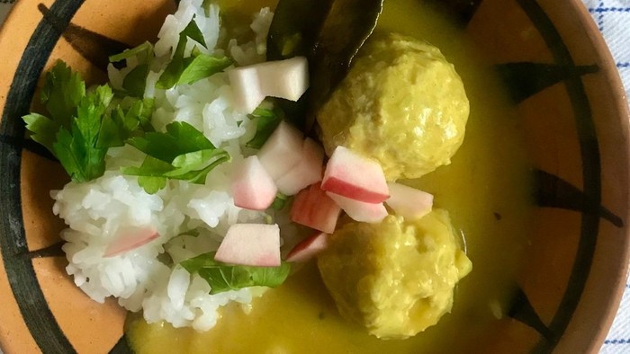 En skål ris toppet med strimlet kål, koriander, radise og gule frikadeller i en cremet sovs.