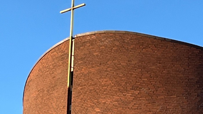 En stor mørk murstenskirke med et guldæret kors på toppen.