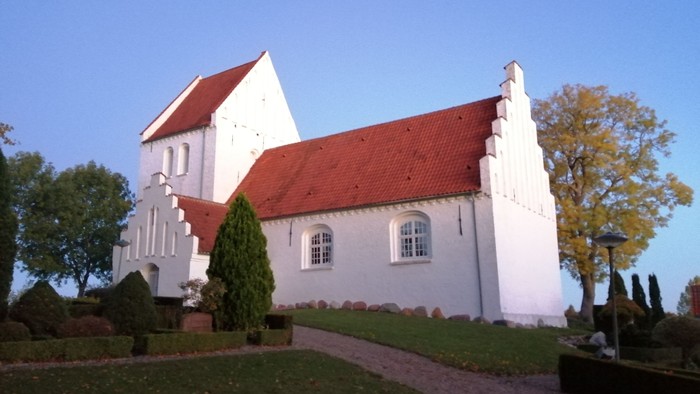 Et hvidt kirkebygning med rødt tag og en smuk have.