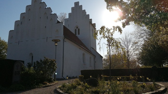 Et hvidt historisk kirkebygningskompleks med en sollysende gennem træerne
