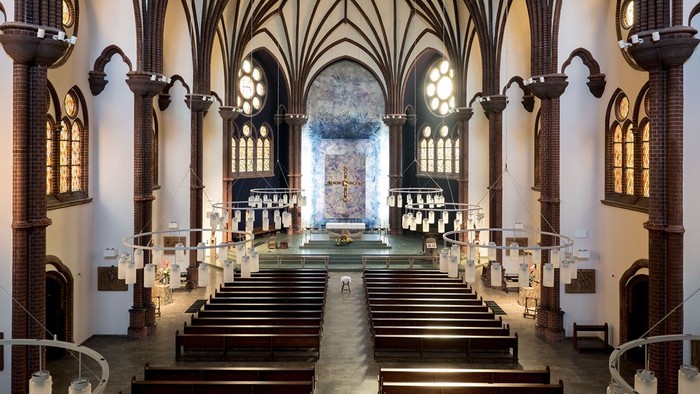 Großzügige Kirchenhalle mit hohen Säulen und Buntglasfenster.