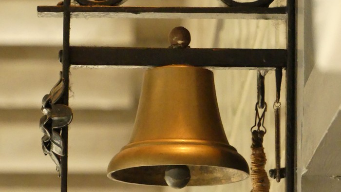 Eine goldfarbene Glocke hängt an einem schwarzen Gestell