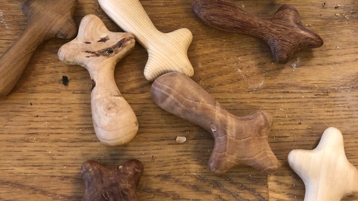 Håndskårne trælegetøj i form af hundeknogler i forskellige færdiggørelsesstadier på en træoverflade.