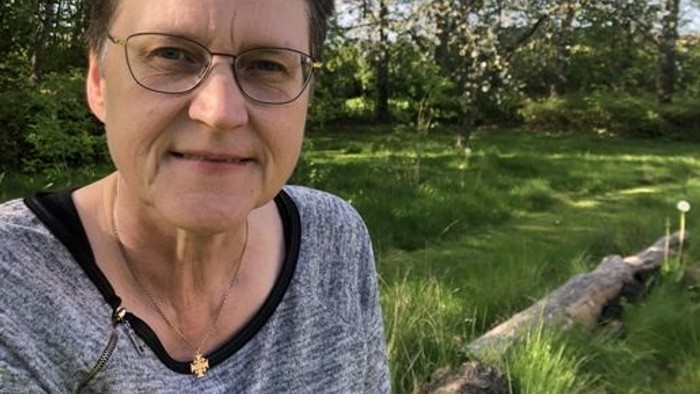 En kvinde sitter udenfor med træer og græs i baggrunden