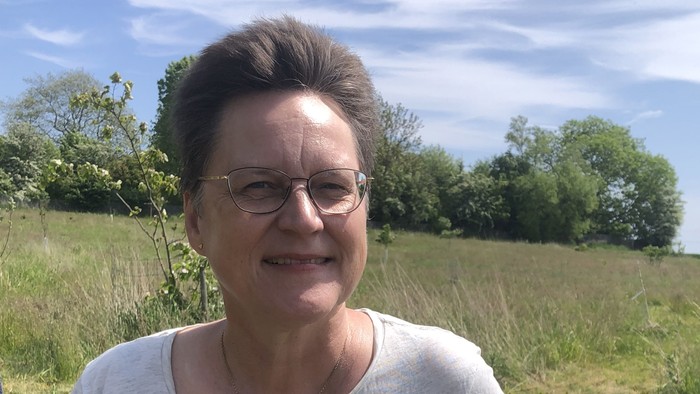 En kvinde sidder på en bænk og smiler.