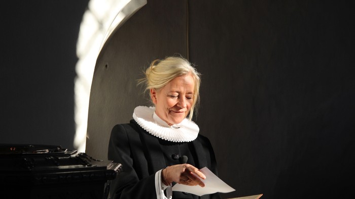 En kvinde i mørkt kostume læser et bog i et lysende rum