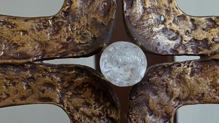 Ein verzierter goldbrauner Metallgegenstand mit einem klaren kugelförmigen Objekt in der Mitte