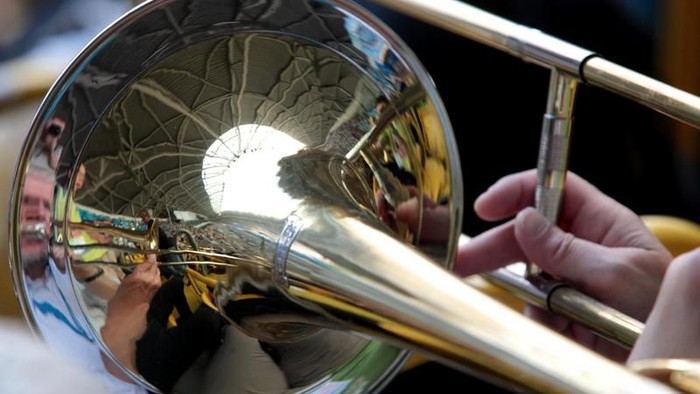 Eine Person, die eine Posaune spielt, wobei ihre Hände auf dem Instrument sichtbar sind.
