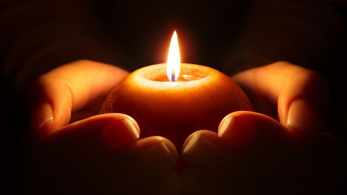 Hände halten eine brennende Kerze im Dunkeln