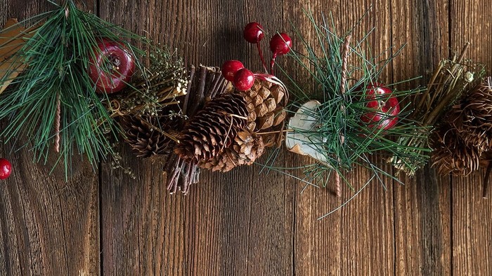 En juledekorationsstang med grønne nåler, nødder og røde bær på et trævæg.