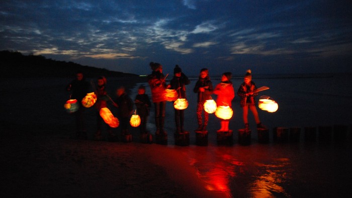 Eine Gruppe von Menschen steht am Strand bei Nacht und hält Laternen.