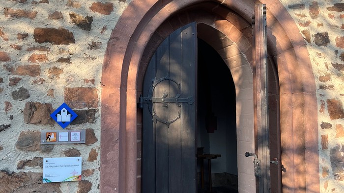 Steingebäude mit bogentüriger Holztür und Laterne darüber.