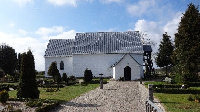 En lille, hvid kirke med smukke omgivelser og stenvej til indgangen
