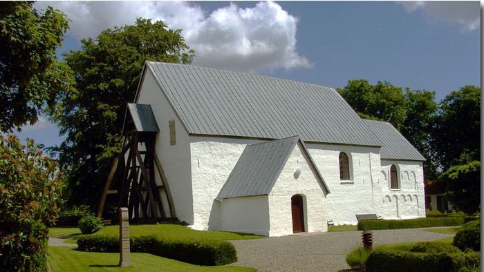 Et hvidt kirkebygning med trætårn og græsplæne foran