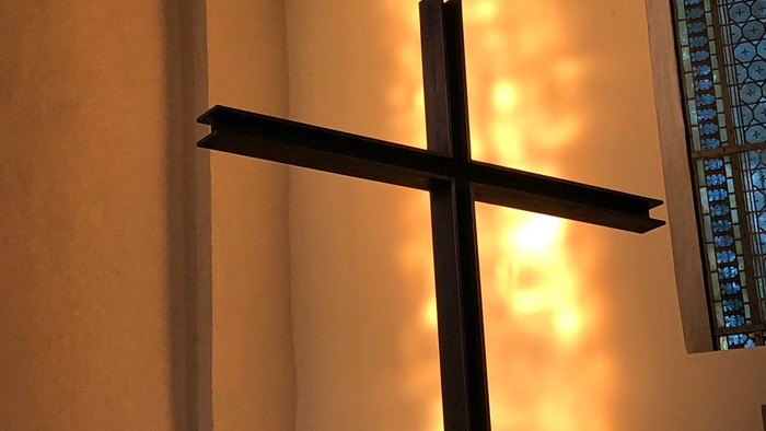 Ein schwarzes Kreuz vor einer hellen Wand.