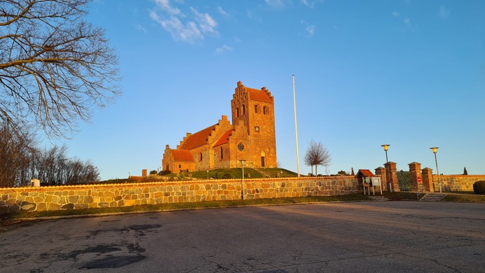 En gammel kirke med tårn og mur, beliggende i solskinn