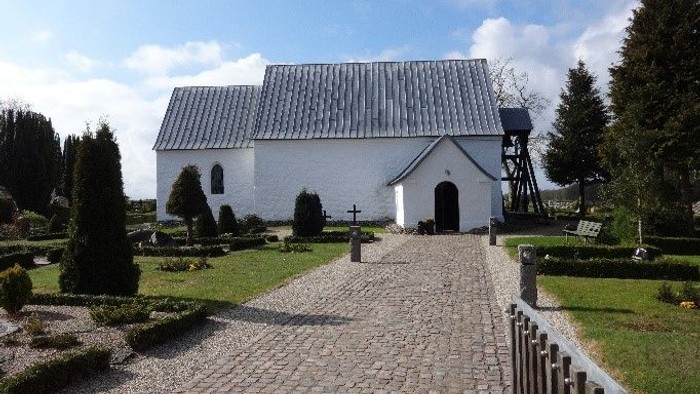 En lille, hvid kirke med smukke omgivelser og stenvej til indgangen