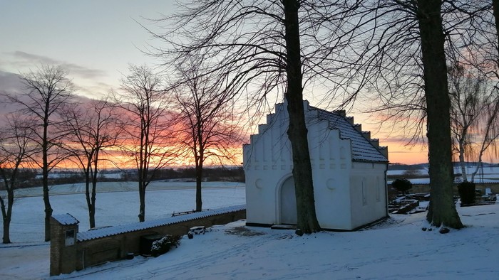 En lille hytte ved en sø i solopgang med sne og træer