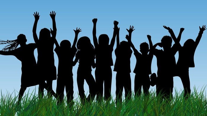 En flok jublende børn, der ses som silhuetter mod den blå himmel. Forrest græs