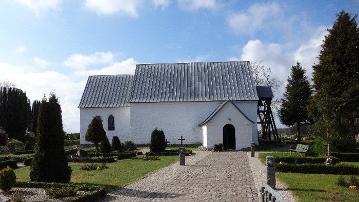 En lille, hvid kirke med smukke omgivelser og stenvej til indgangen