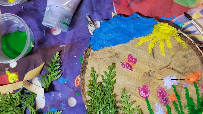 Bunter bemalter Holzuntersetzer mit einer verspielt gestalteten Wüstenlandschaft mit Blumen, Kakteen und einer Sonne.