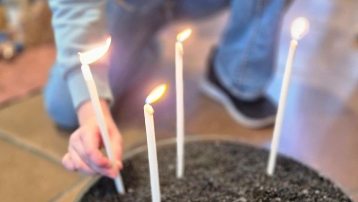 Fünf brennende Kerzen, die in einem runden Behälter mit dunkler Erde oder Sand platziert sind.