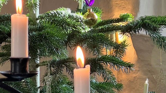 En lille julestænde med tre lysende lysekønge og lilla pynt.