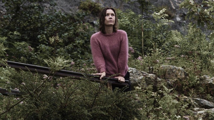 En person, der sidder på en klippeafsats omgivet af tæt grønt og forrevne klipper.