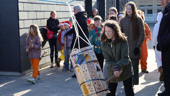 En gruppe mennesker går sammen og bærer et stort, farverigt træfuglehus på en vogn udendørs.