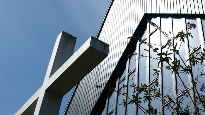 Moderne skulptur sat over for en slank, reflekterende glas- og metalhøjhus under klar himmel.