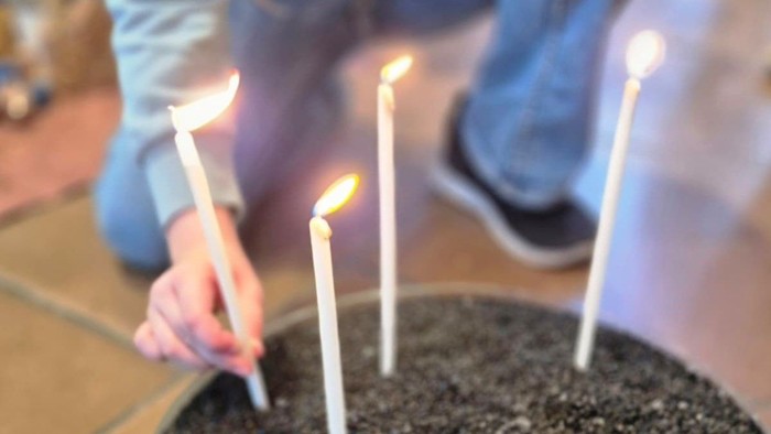 Fünf brennende Kerzen, die in einem runden Behälter mit dunkler Erde oder Sand platziert sind.