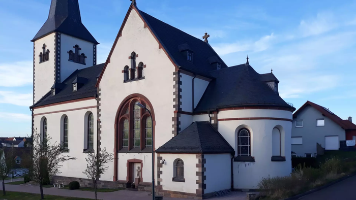 Eine malerische weiße Kirche mit hohem Turm und Bogenfenstern vor einem klaren Himmel.