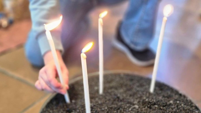 Fünf brennende Kerzen, die in einem runden Behälter mit dunkler Erde oder Sand platziert sind.