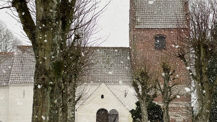 En snødekkede kirke med tårn og træer.