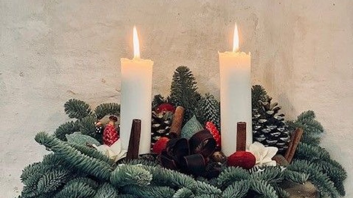 En juledekorasjon med tre lysende lygter, grønne nåler og røde kugler på en træskive.