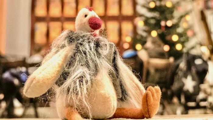 Ein Stofftier-Huhn, das auf einer Fensterbank sitzt, mit Weihnachtsdekoration im Hintergrund.