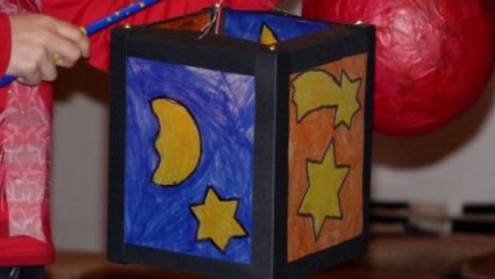 Ein Kind hält eine selbstgebastelte Laterne mit Mond- und Sternmotiven.