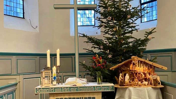 In der Kirche steht ein geschmückter Weihnachtsbaum neben einem Krippenspiel.