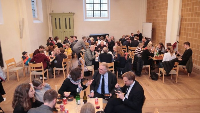 Eine Gruppe von Menschen sitzt an Tischen in einem Raum und isst.