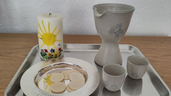 Zeremonielle Schale mit Kerze, Kelch, Hostien und kleinen Bechern auf einer Holzfläche.