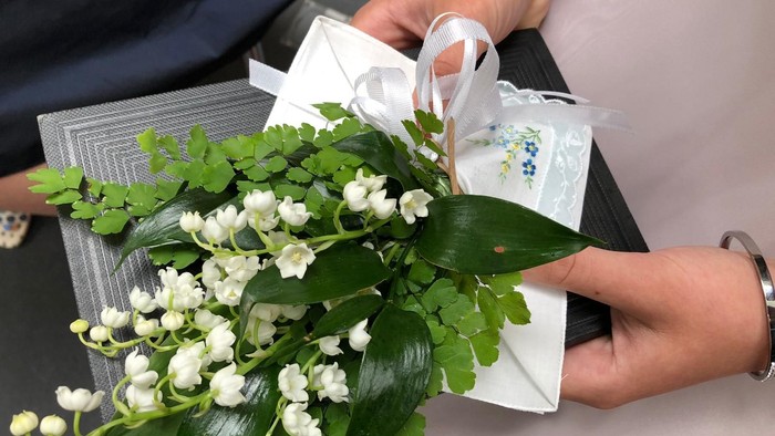 Eine Person hält einen Strauß weißer Blumen und eine Geschenkbox.